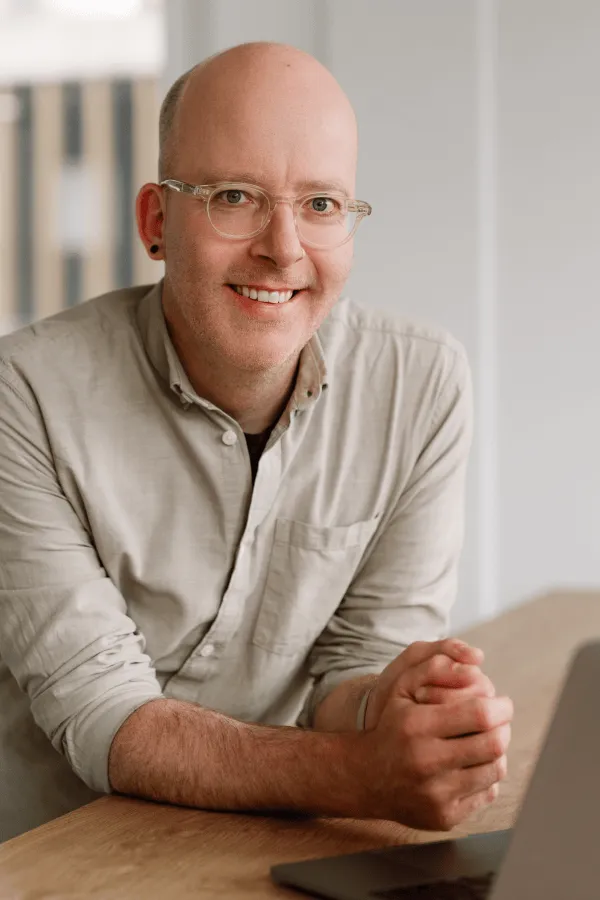 Roland Beyeler leaning on a table in the office, wearing a bright shirt and smiling at the camera.