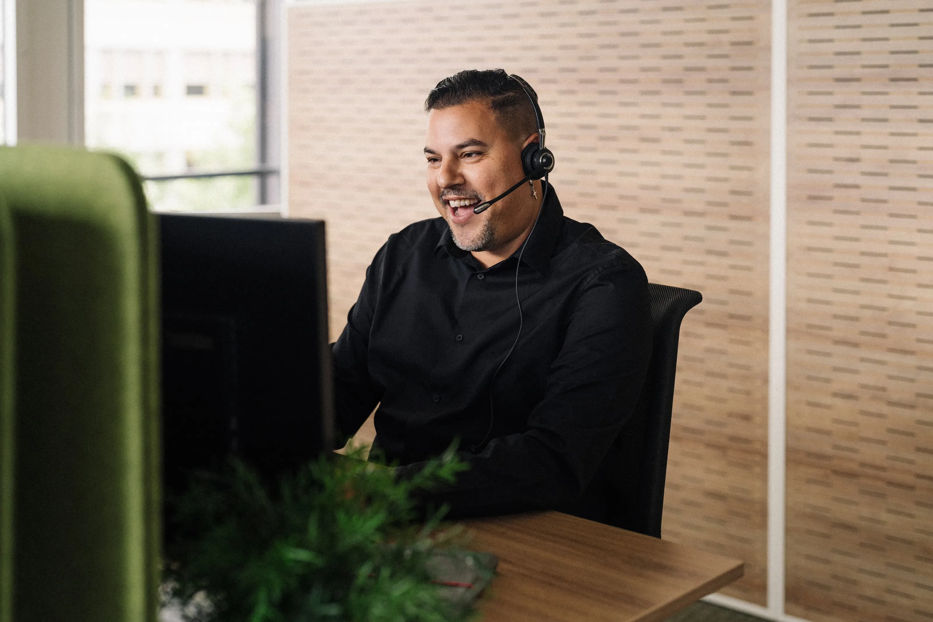 Ricardo Perrini wearing a headset while sitting in front of a screen in the office and speaking with a smile during a customer meeting.