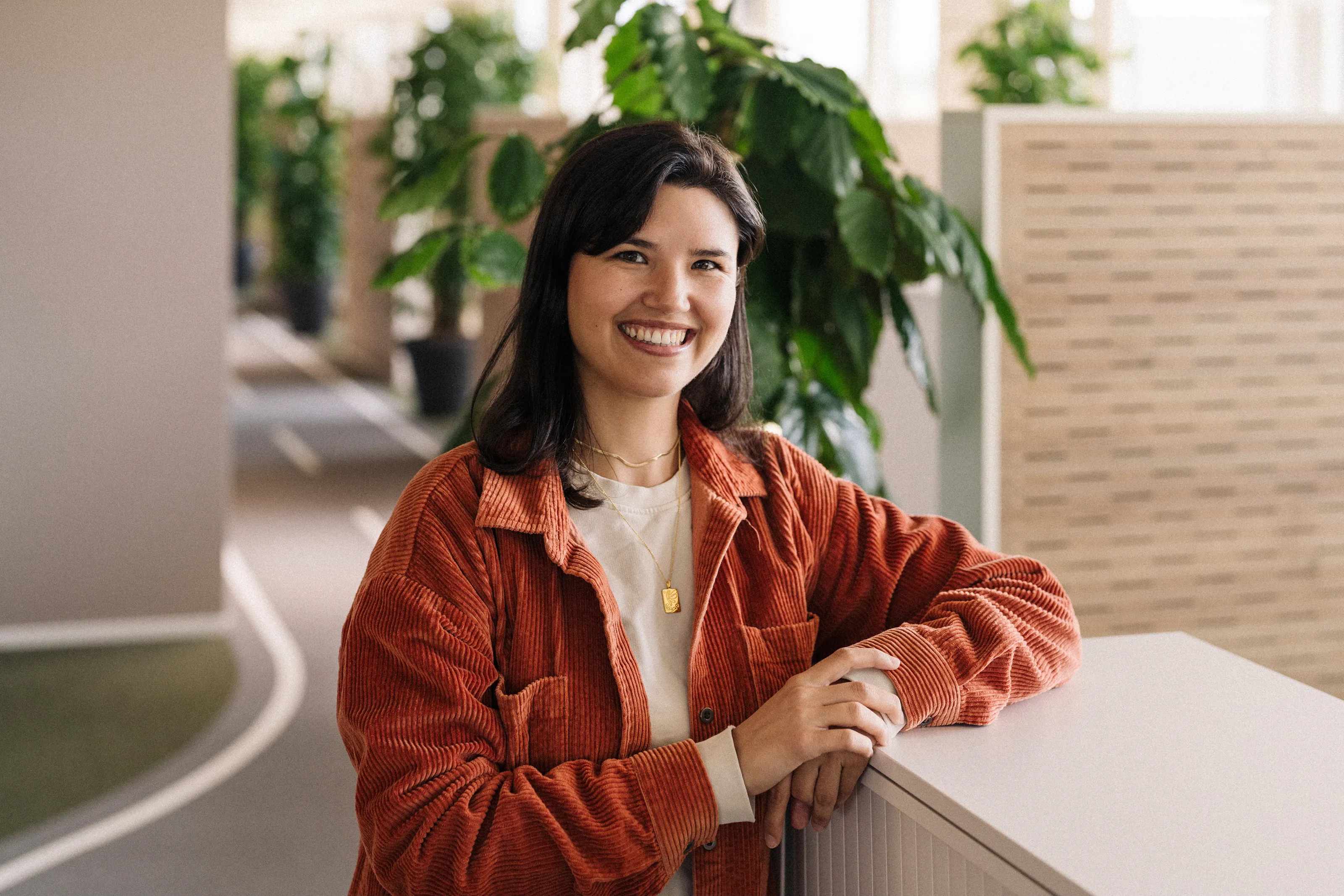 Mirjam Kara in a red jacket, smiling and leaning against a piece of furniture in the Mobility office.