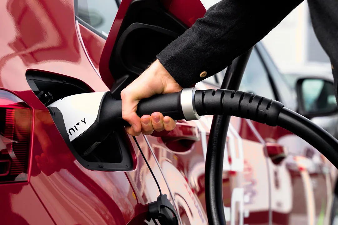Person plugs a charging cable into an electric car at a public charging station and charges the vehicle with electricity.