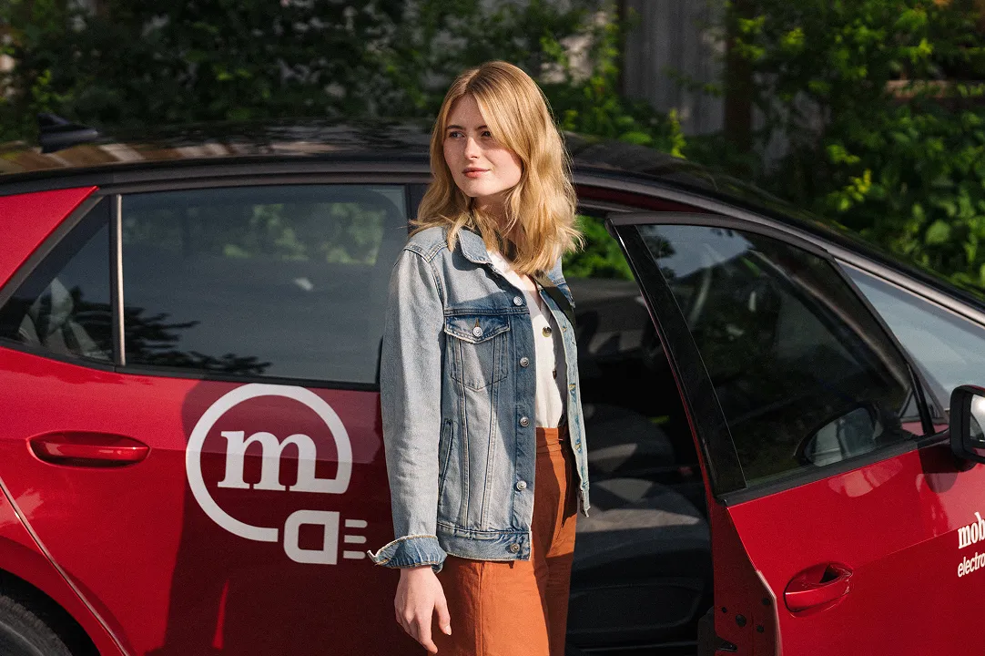 Woman standing next to a red Mobility sharing car with the door open and using shared mobility in everyday life.