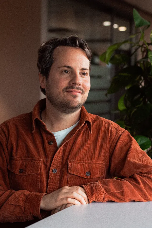 Markus Broder sitting at a table in the office and looking to the side with a smile.