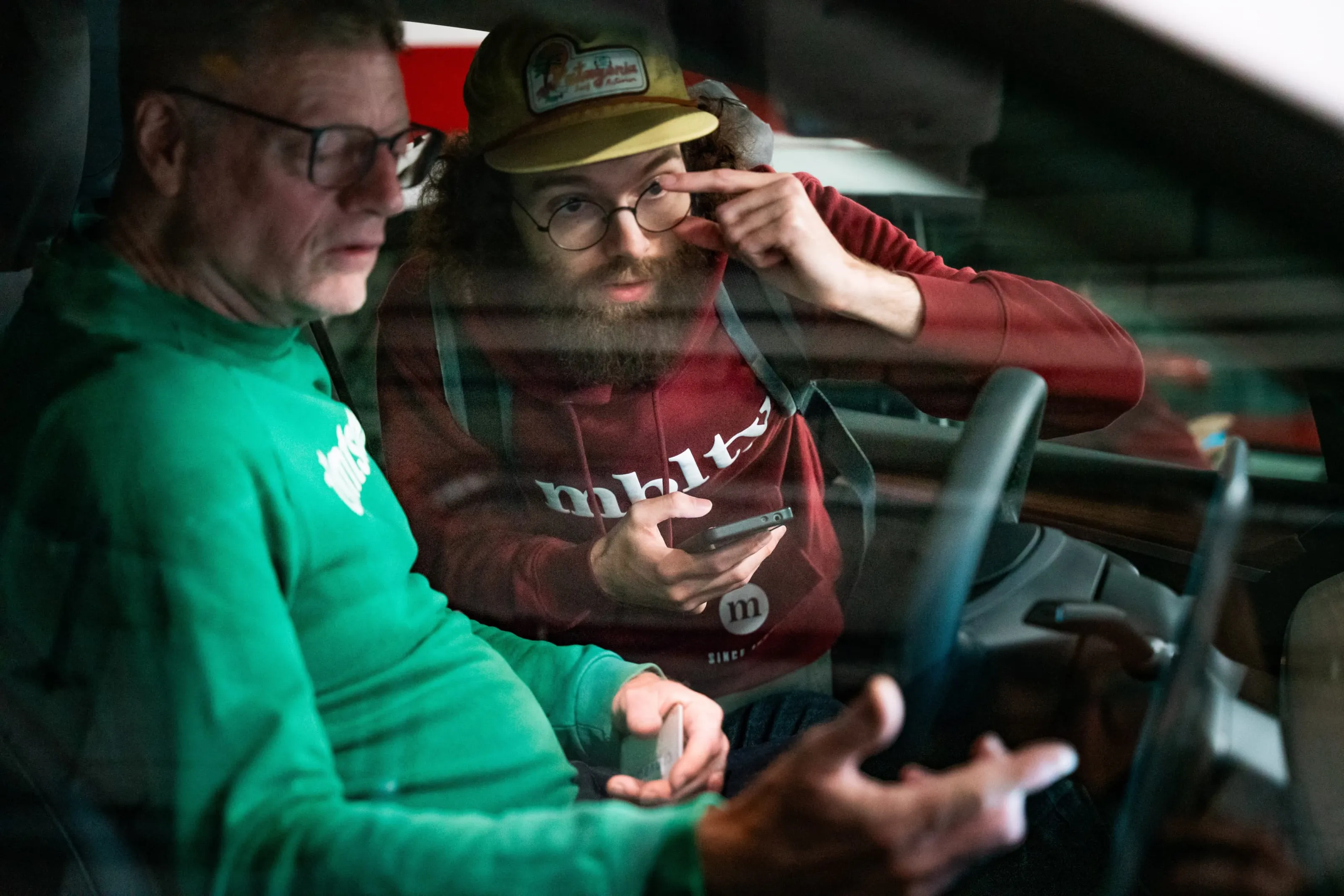 Two men sitting in the car looking at a smartphone together while discussing something.
