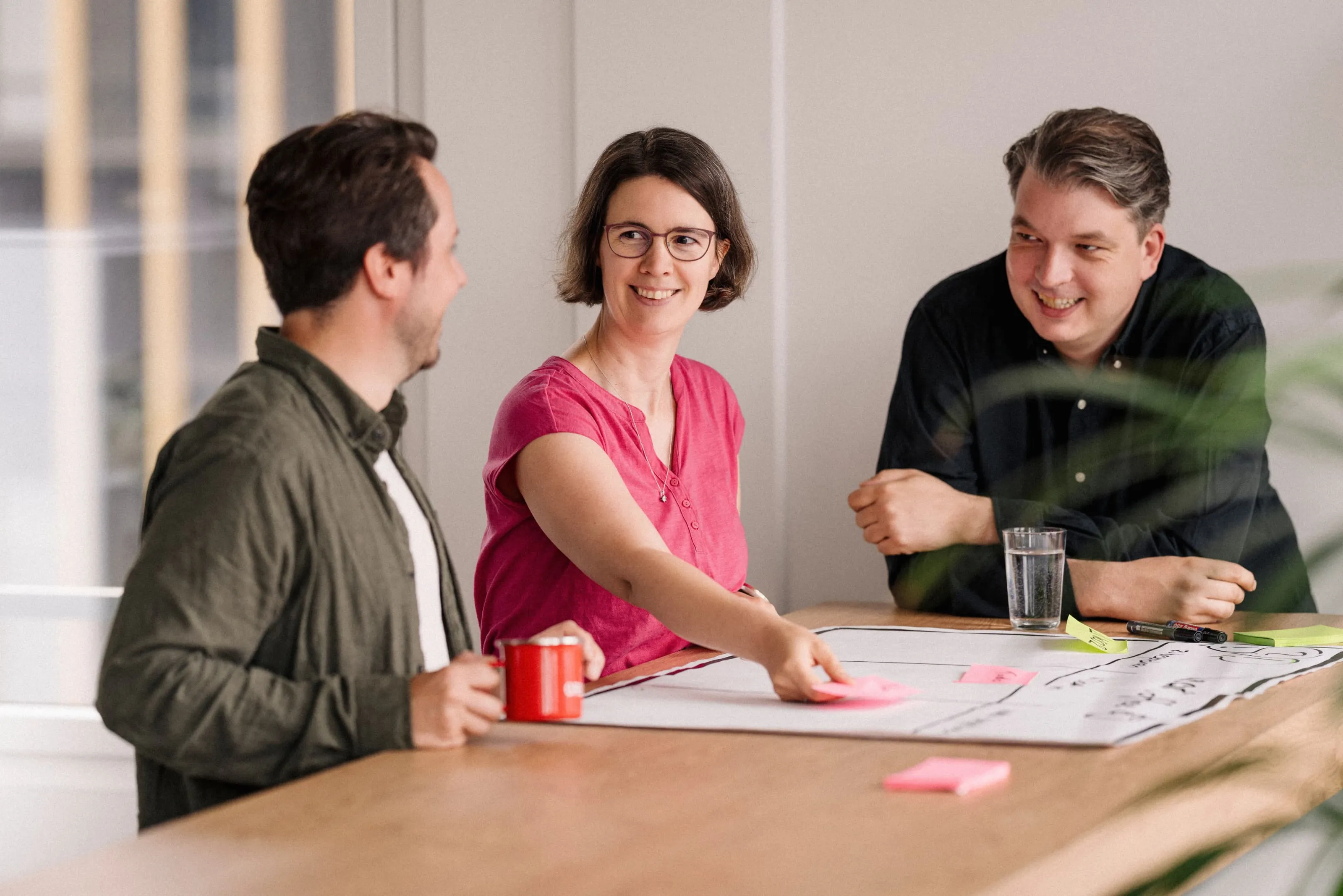 Three people discussing ideas at a table with post-its during a workshop in the office.